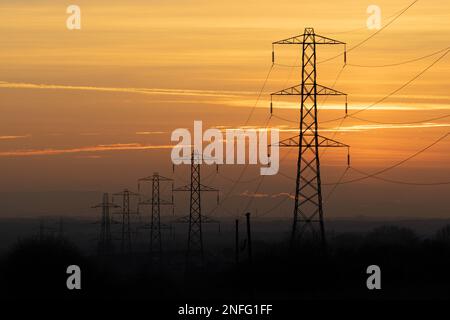 Row of electricity pylons silhouette against orange sky at sunset, UK. Theme of energy usage, power, bills, rising costs, power grid Stock Photo