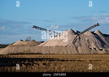 Heaps of sand near a gravel plant with two conveyor in the evening sun Stock Photo
