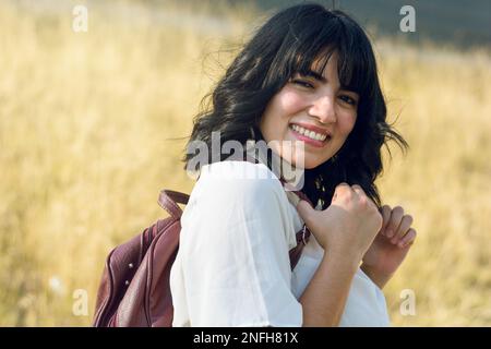 happy young college woman back to class, standing outdoors smiling looking at the camera, dressed in white and carrying a backpack. Stock Photo