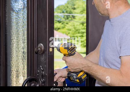 During construction of new home carpenter worker installs new lock on front door using screwdriver Stock Photo