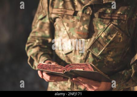 Soldier dressed in camouflage uniform holding a bible in his hand. Soldier reading and meditating on God's word Stock Photo