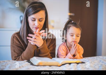 mother and her little girl praying at the edge of the bed in the morning Stock Photo