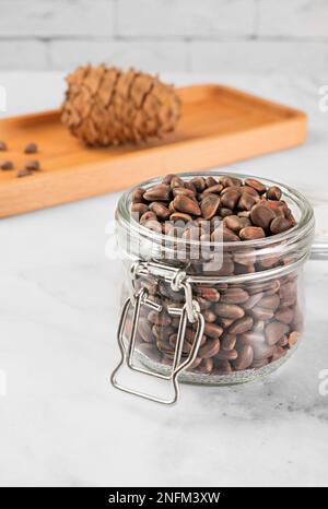 Pine nuts in a jar and a pine cone in the kitchen on a light background. The concept of organic food and protein food Stock Photo