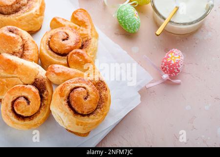 Easter breakfast Holliday concept. Easter bunny buns rolls with cinnamon made from yeast dough with orange glaze, easter decorations, colored eggs on Stock Photo