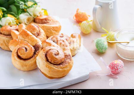 Easter breakfast Holliday concept. Easter bunny buns rolls with cinnamon made from yeast dough with orange glaze, easter decorations, colored eggs on Stock Photo