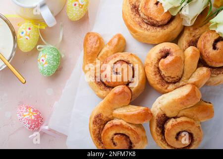 Easter breakfast Holliday concept. Easter bunny buns rolls with cinnamon made from yeast dough with orange glaze, easter decorations, colored eggs on Stock Photo