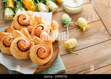 Easter breakfast Holliday concept. Easter bunny buns rolls with cinnamon made from yeast dough with orange glaze, easter decorations, colored eggs on Stock Photo
