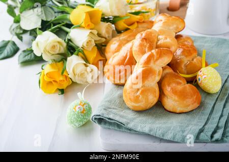 Easter breakfast Holliday concept. Easter bunny buns rolls with cinnamon made from yeast dough with orange glaze, easter decorations, colored eggs on Stock Photo