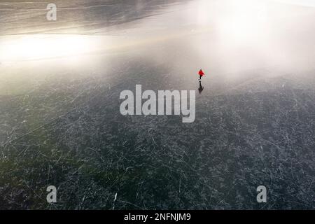 Aerial view of a Woman in red ice skating in nature on a beautiful natural frozen Cerknica lake on a beautiful winter day, Slovenia Stock Photo