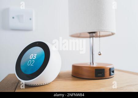 Bedside smart device showing the local time. Located next to a beside lamp with USB charging ports Stock Photo