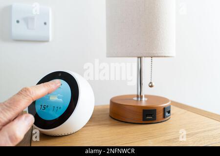 Owner checking the weather forecast on his smart device located on a bedside table. Note the table lamp with USB charge ports. Stock Photo