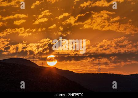 setting sun behind hill with pylons Stock Photo