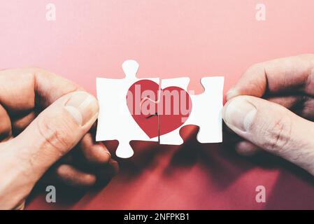 hands connecting or disconnecting jigsaw puzzle pieces with red heart, love or broken heart concept Stock Photo