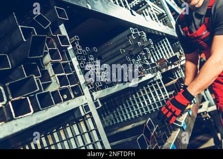 Metalworking Warehouse Worker Arranging Metal Profiles and Square Tubes on Storing Shelves. Industrial Theme. Stock Photo