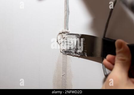 Worker fixing cracks on ceiling, spreading plaster using trowel.plastering cement on wall. Builder applying white cement to a crack in a wall with a Stock Photo