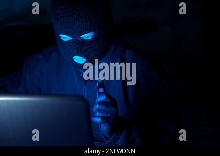 Masked hacker stealing data and personal identity information off laptop  Stock Photo