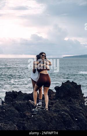 Two female friends embrace standing on a rock. Farewell. Friendship. Vacation. Hug Stock Photo