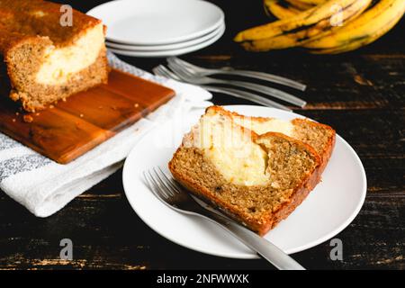 Slices of Cream Cheese-Filled Banana Bread on a White Plate: Slices of banana bread with ripe bananas in the background Stock Photo