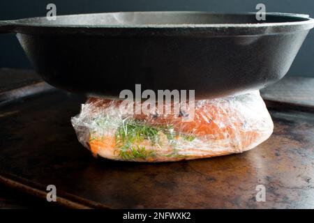 Making Homemade Lox with Salmon, Spices, and Salt: Salted salmon fillets wrapped in plastic and weighted with a cast iron skillet Stock Photo