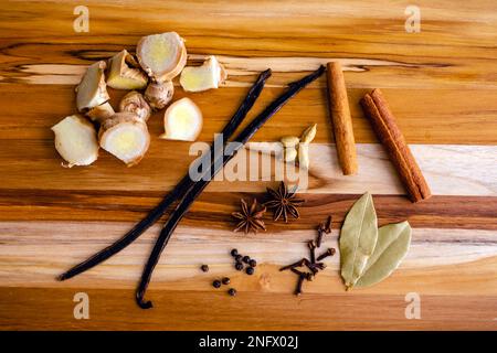 Fresh and Dried Spices on a Wooden Cutting Board: Split vanilla bean, chopped ginger, and other dried spices on a wood background Stock Photo