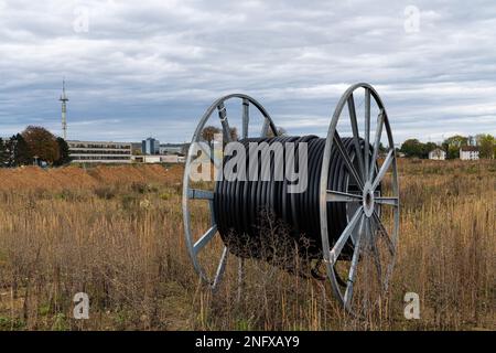 Large metal cable reel with black plastic cable on a vacant lot. The gray sky is covered with clouds. Stock Photo