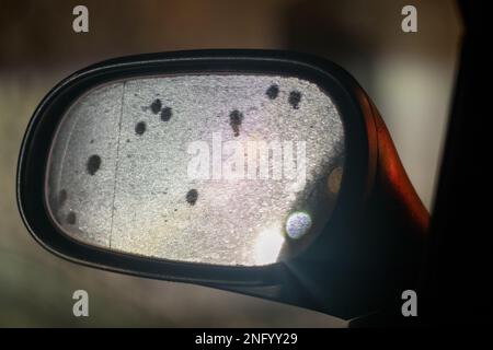 Lef side mirror on car at night reflects a city lights and  water drops. Close up view of bright blurred background. Stock Photo