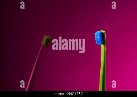 Green and pink toothbrushes on vibrant pink background Stock Photo