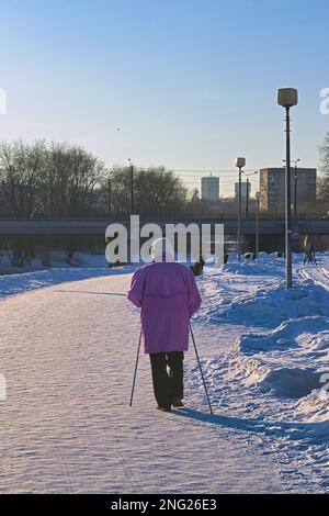 An elderly woman is engaged in nordic walking in the park. Stock Photo