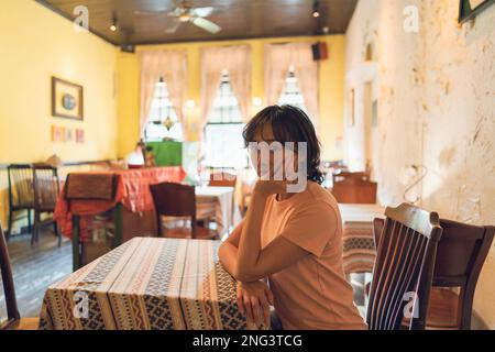 A woman sat in a vintage style cafe. The camera caught her side face while she looked at the camera. Stock Photo