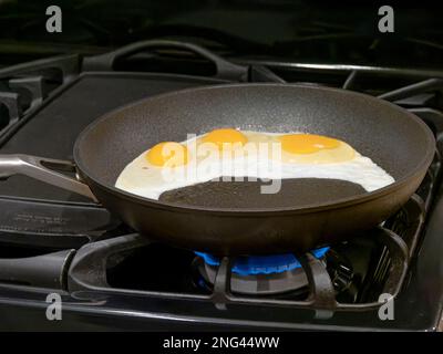 Eggs frying in a skillet or frying pan for cooking on a gas stove or stovetop in a home in the USA. Stock Photo