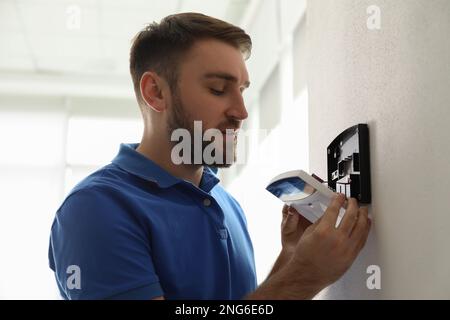 Man installing home security system on white wall in room Stock Photo