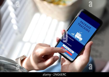 Woman tracking parcel via smartphone indoors, closeup Stock Photo