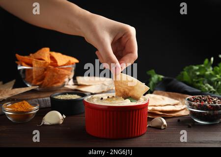 Woman dipping pita chips into hummus at wooden table, closeup Stock Photo