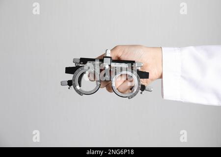 Ophthalmologist holding trial frame on light background, closeup Stock Photo