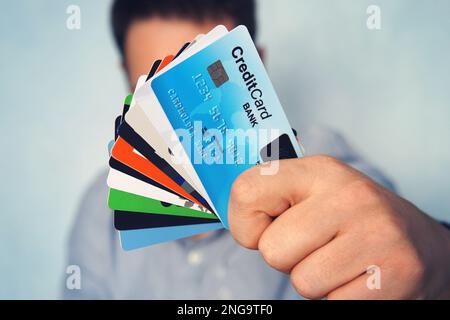 Young man in light blue shirt showing many types of credit cards. Businessman in casual wear holding in hand various payment cards. Stack of cards wit Stock Photo