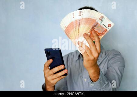 Smartphone and money. young man is holding a smartphone and a large wad of 5000 ruble bills. earnings with the help of the phone. Stock Photo