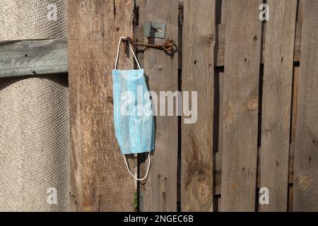 medical mask hanging on a hook an old wooden gate in Ukraine on the street during Stock Photo