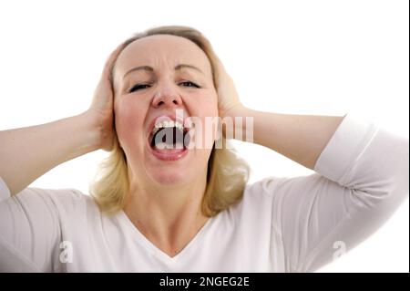 a close horizontal studio photo of a red-haired woman screaming loudly clutching her head from shock. Woman is screaming and covering hew ears with hands High quality photo Stock Photo