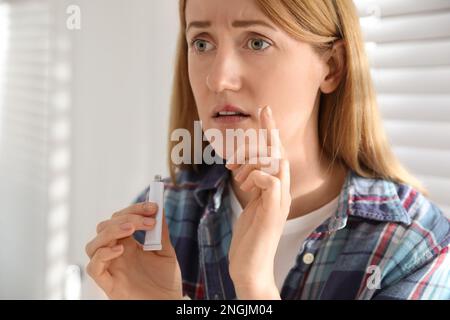 Upset woman with herpes applying cream on lips indoors Stock Photo