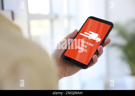 Woman tracking parcel via smartphone indoors, closeup Stock Photo