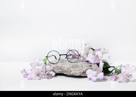 Funny round glasses from the sun or for vision, on a podium stone with pink flowers, on a table, on a white gray background. Creative glasses advertis Stock Photo