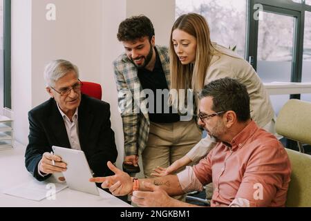 Four colleagues, two juniors and two seniors working on a same project together in the office Stock Photo