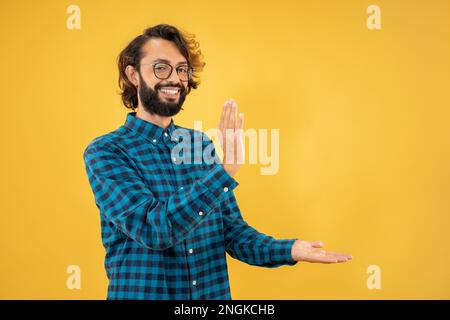 Young man standing over isolated yellow background pointing aside with hands open palms showing Stock Photo