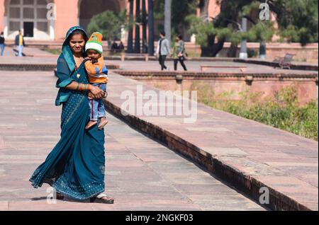 A young Indian Hindu woman dressed in a beautiful green traditional saree holding her young one year old son outside a public monument in Agra India. Stock Photo