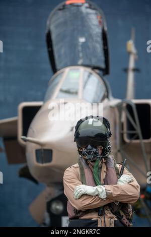 Fighter pilot, RAF, standing with fighter Jet ready for a combat mission wearing flying helmet, suit and dark visor with oxygen mask Royal Air Force. Stock Photo