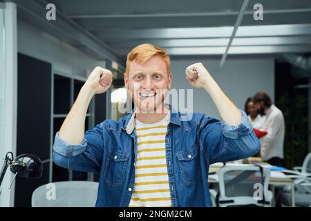 Young red-haired programmer or businessman in modern office looking at camera and smiling. Stock Photo