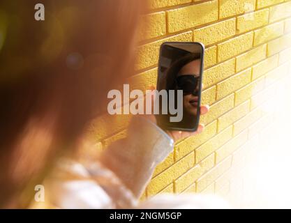 Woman face reflection in screen of mobile phone against brick wall. Stock Photo