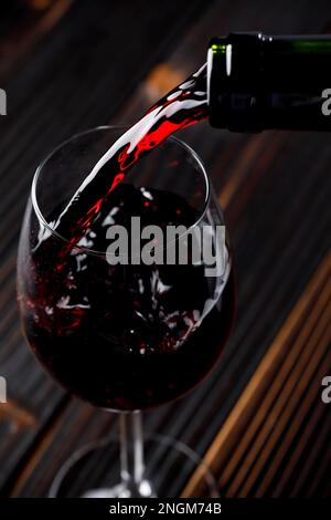 Red wine pouring  in glass on wooden table Stock Photo