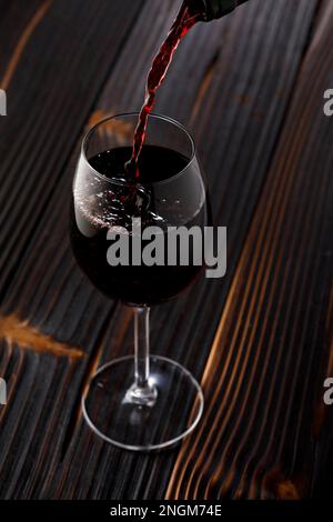 Red wine pouring  in glass on wooden table Stock Photo