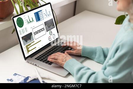 Laptop Computer Showing Statistical Infographics Stands on a Desk in the Living Room. In the Background Cozy Living Room. Stock Photo